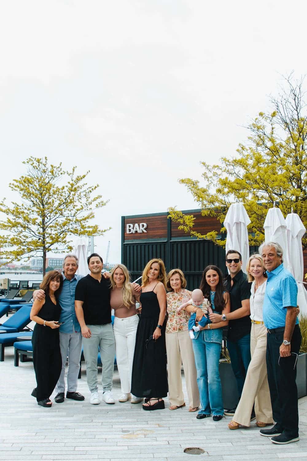 Family celebrating together at a waterfront after a surprise proposal, photographed by Create With Amy in Baltimore, Maryland